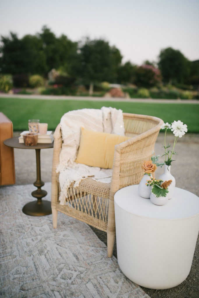 Wicker accent chair with side table adorned with bud vases designed by wedding rental company Avenue Twelve